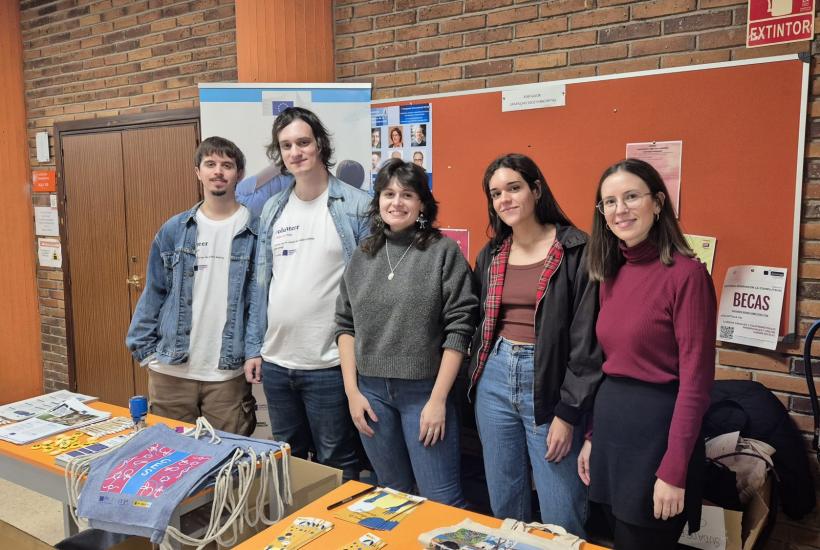 Cinco jóvenes junto a una mesa con merchandising e información